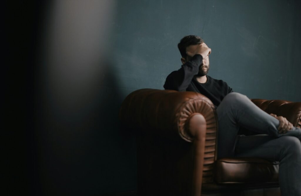 a man holds his head while sitting on a sofa: Depression Counseling