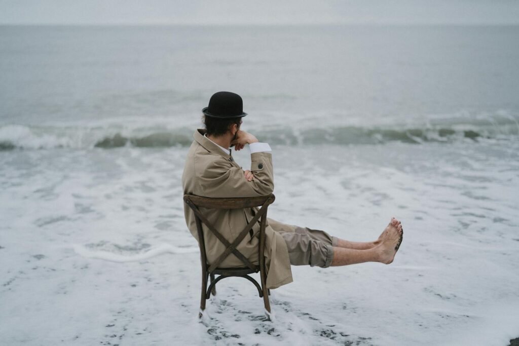 A New Chapter: Addiction Therapy in Chicago for Healing and Hope 1 Man in coat and hat sitting on a chair at the edge of the ocean, lost in thought. A New Chapter: Addiction Therapy in Chicago for Healing and Hope