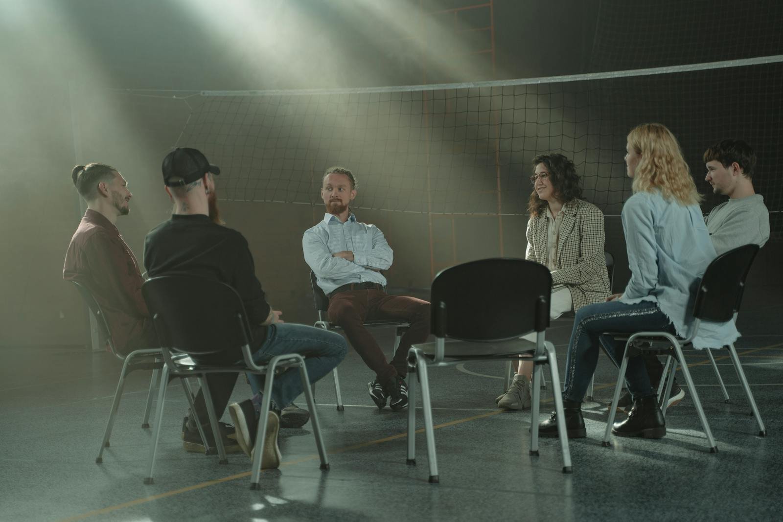 A group therapy session with six adults seated in a circle, discussing support and mental health.